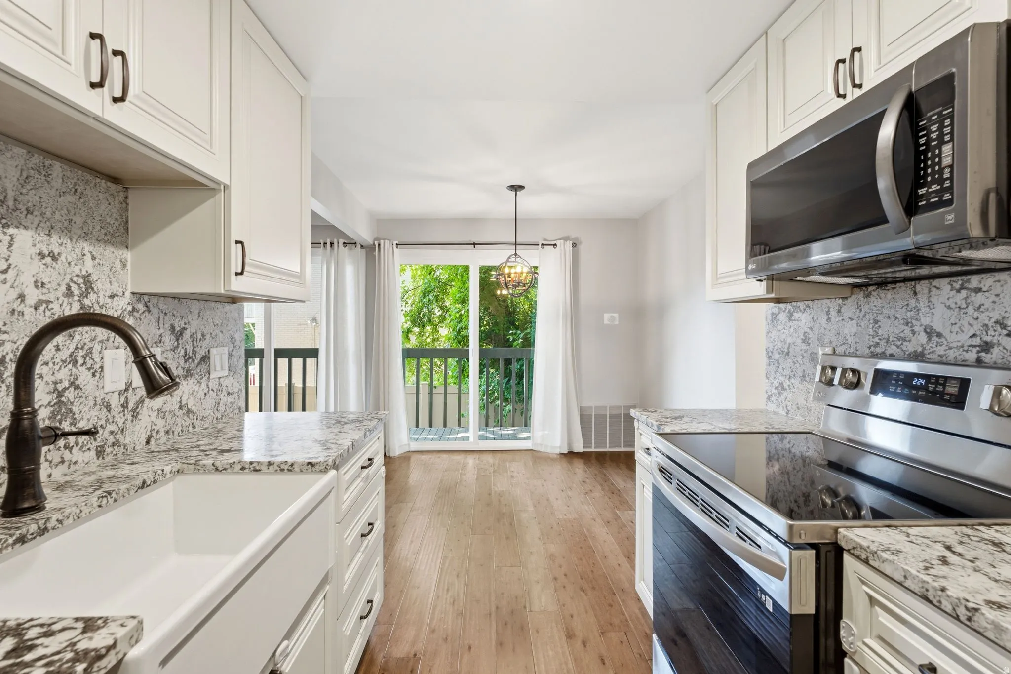 White cabinetry with dark hardware, stone countertops with matching backsplash, stainless steel appliances, a farmhouse sink, and wood-finish flooring