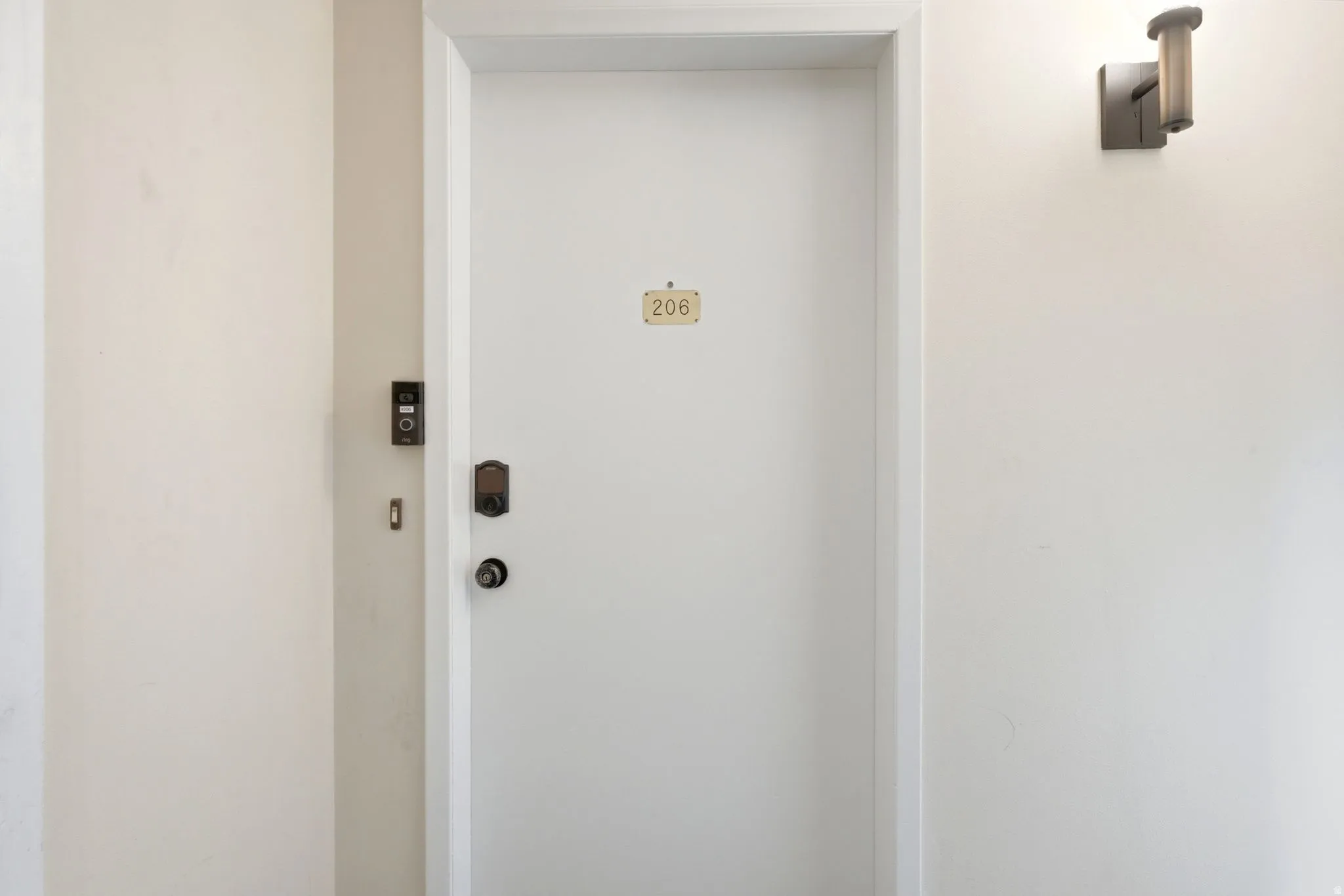 Entry door with digital smart lock, modern wall sconce, and doorbell system
