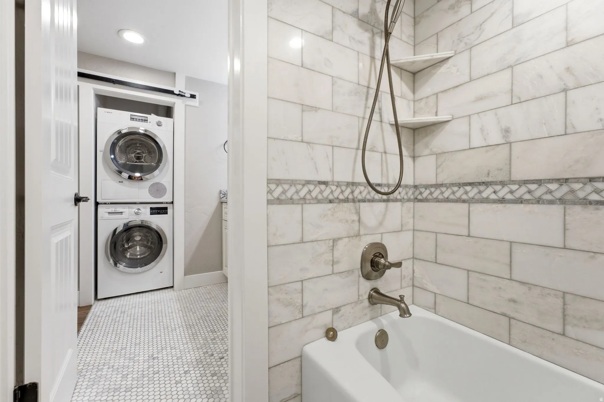 Bathroom featuring a white bathtub with brushed nickel fixtures, subway tile shower surround with mosaic accent, and integrated corner shelves