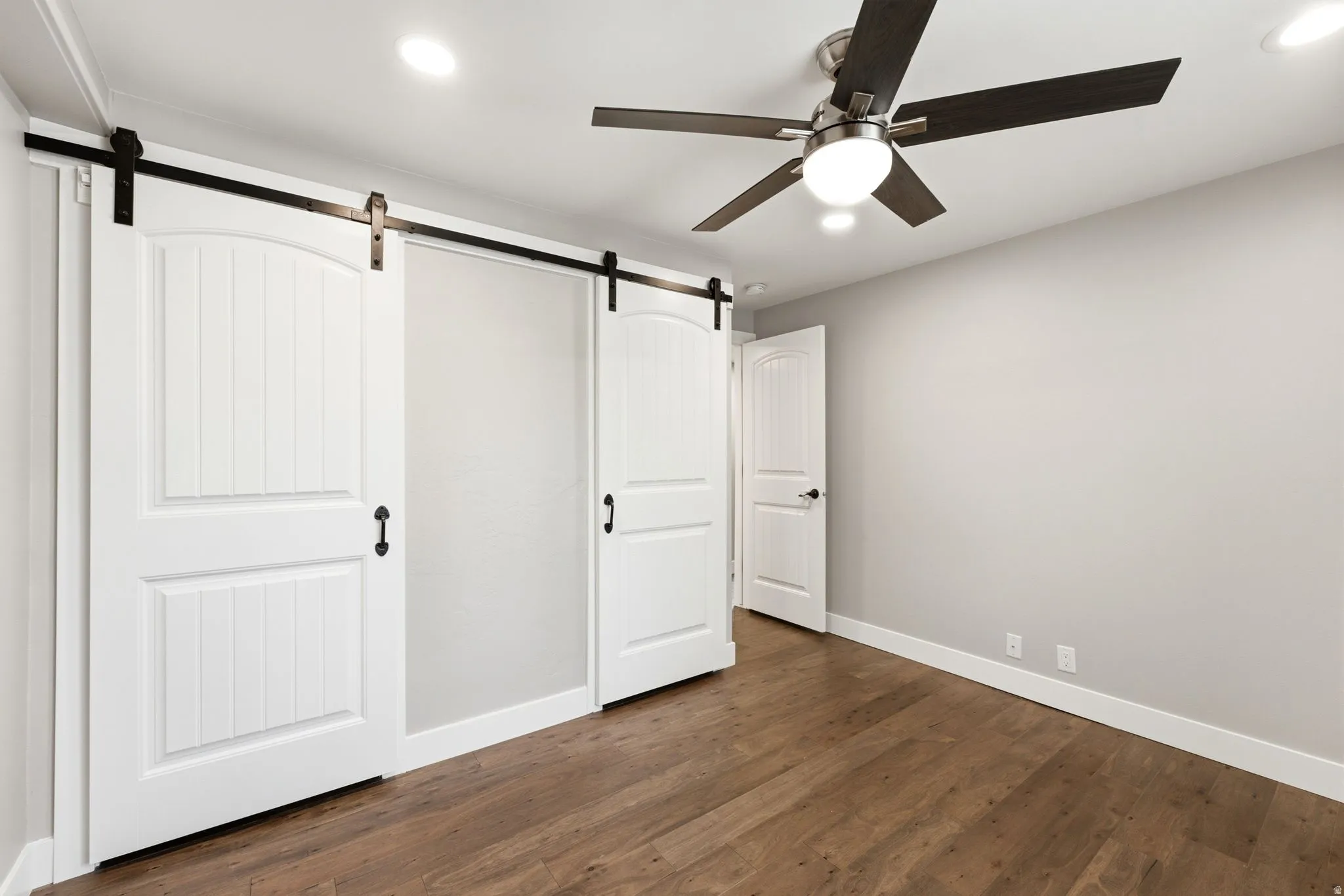 Wood-finish flooring, recessed lighting, ceiling fan with integrated light, white paneled doors, and barn door hardware