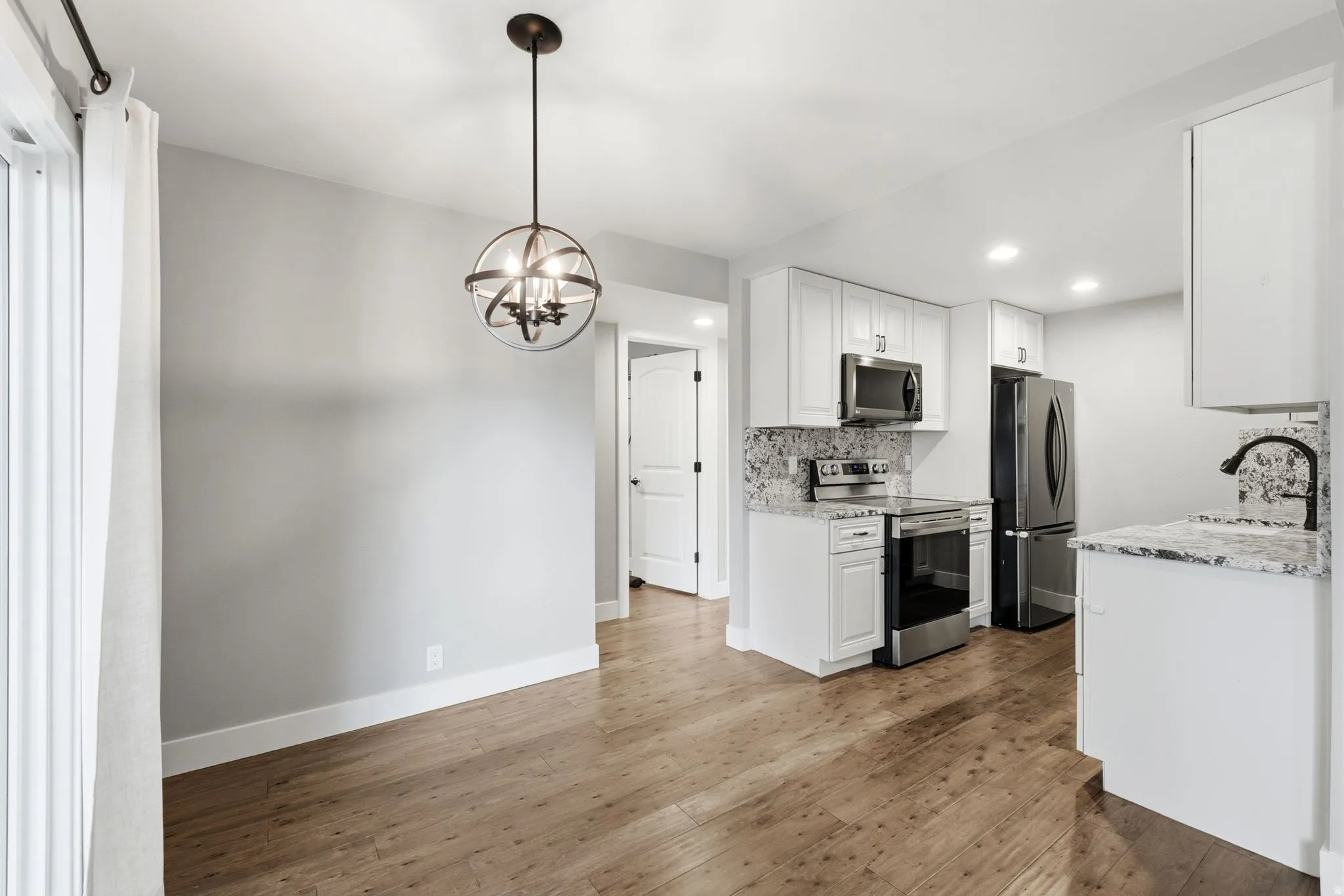 Wood-finish flooring, white cabinetry, stainless steel appliances, speckled countertops, and a modern orb chandelier