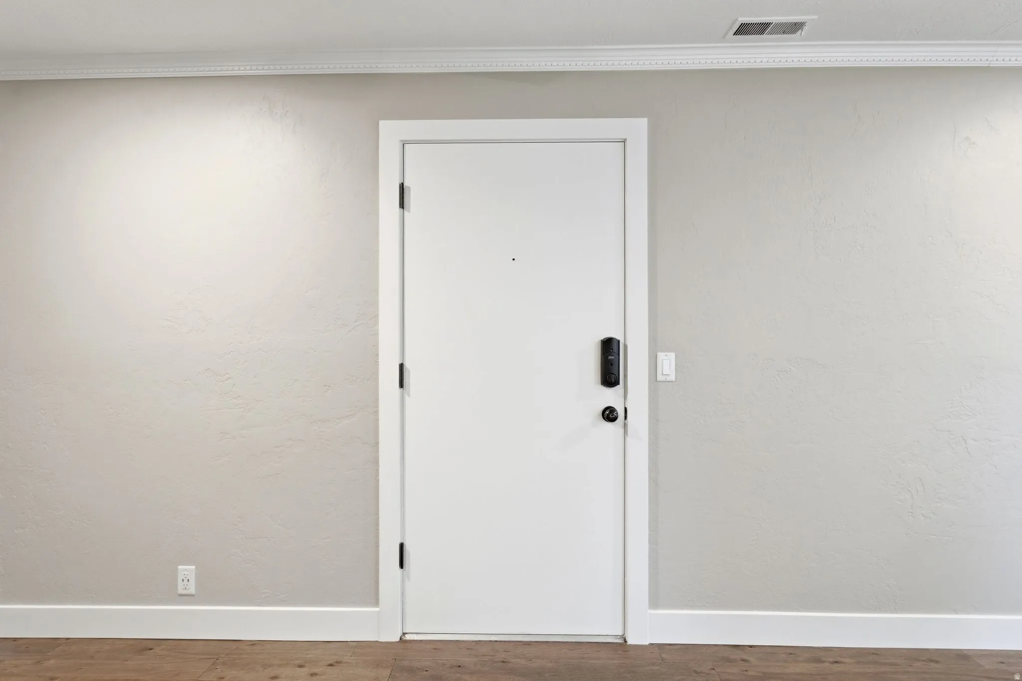 White interior door with smart lock entry system, crown molding, and wood-finish flooring