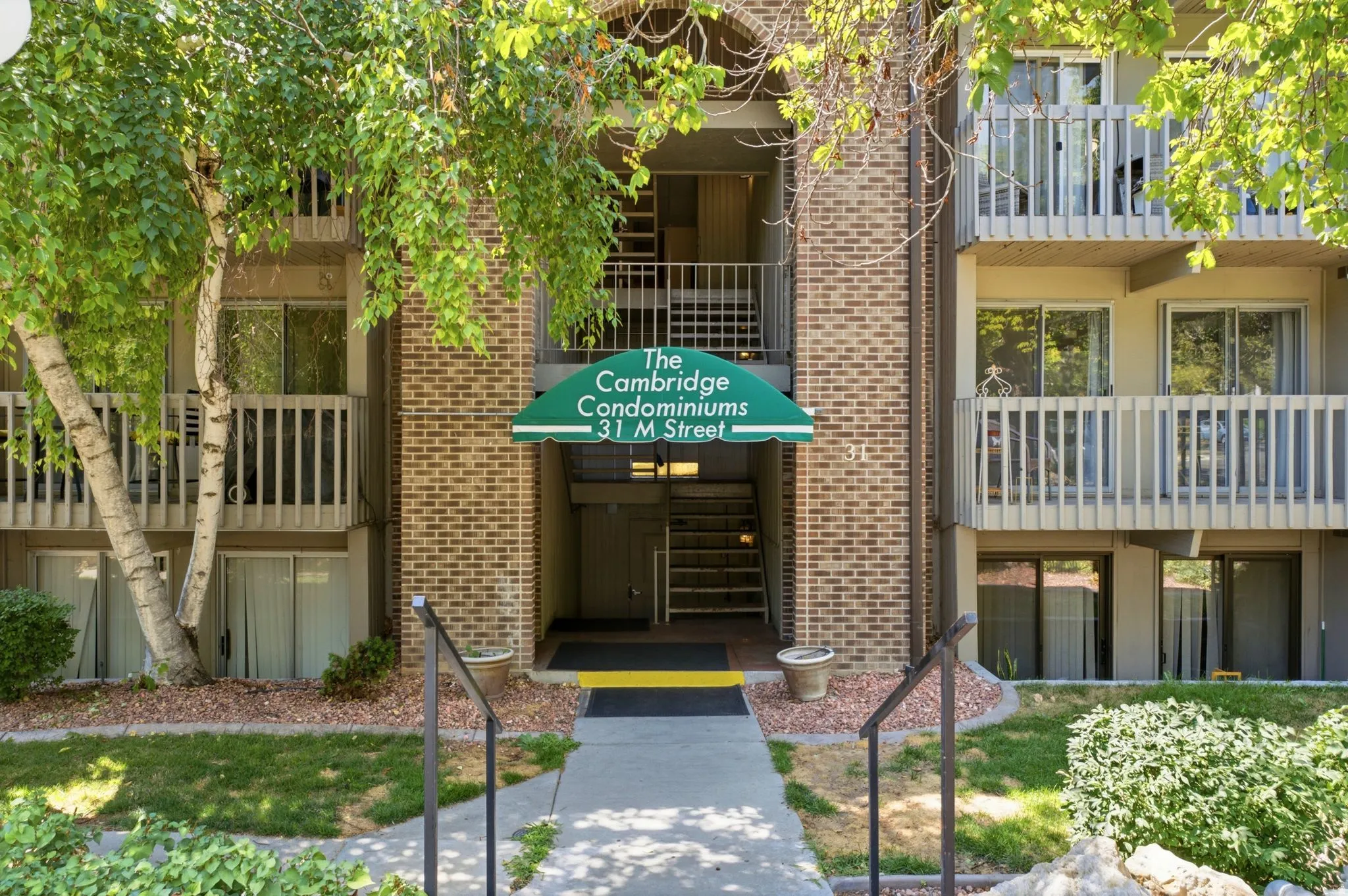 Brick exterior featuring a green entrance awning, multiple balconies, and mature landscaping