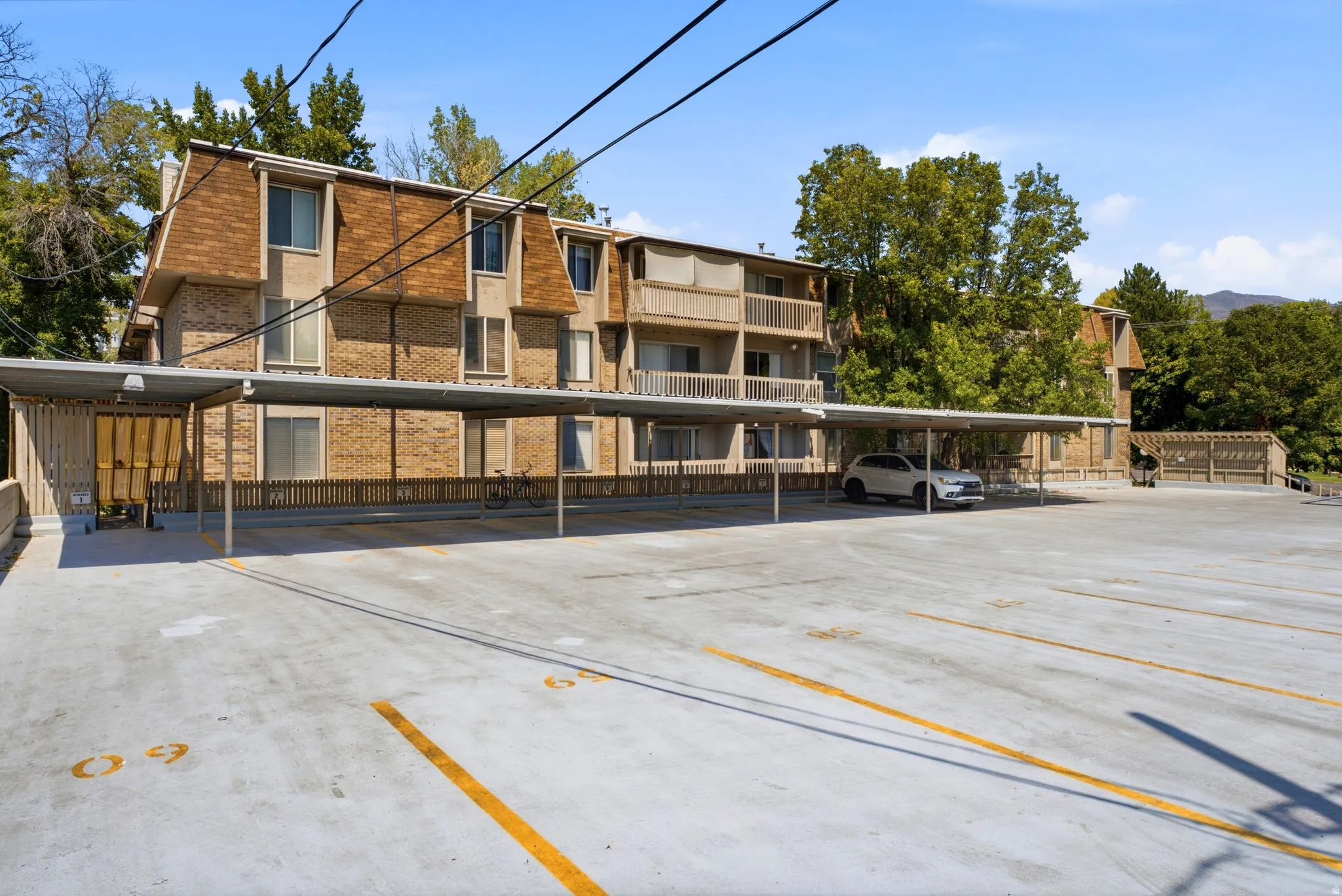 Expansive paved parking area with covered parking structures, brick building exterior, and multiple balconies