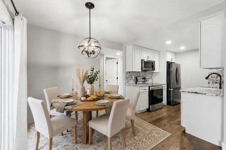 Kitchen featuring white cabinetry, stainless steel appliances, granite countertops, and wood-finish flooring