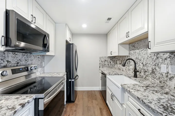 White shaker-style cabinetry, granite countertops, wood-finish flooring, stainless steel appliances, and a farmhouse sink