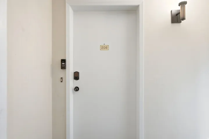 Entry door with digital smart lock, modern wall sconce, and doorbell system