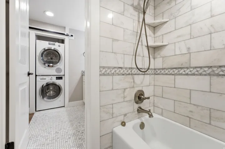 Bathroom featuring a white bathtub with brushed nickel fixtures, subway tile shower surround with mosaic accent, and integrated corner shelves