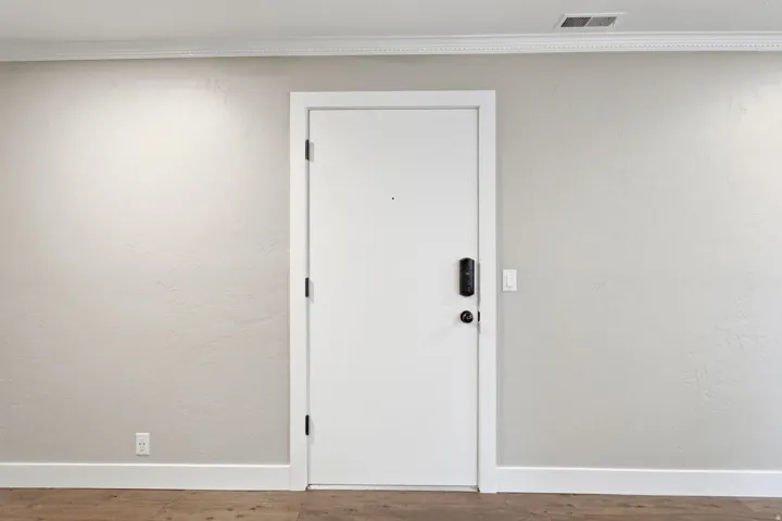 White interior door with smart lock entry system, crown molding, and wood-finish flooring