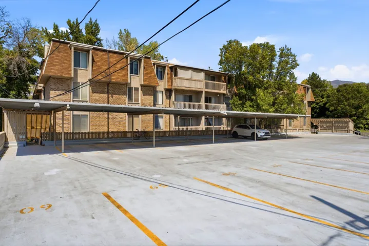 Expansive paved parking area with covered parking structures, brick building exterior, and multiple balconies