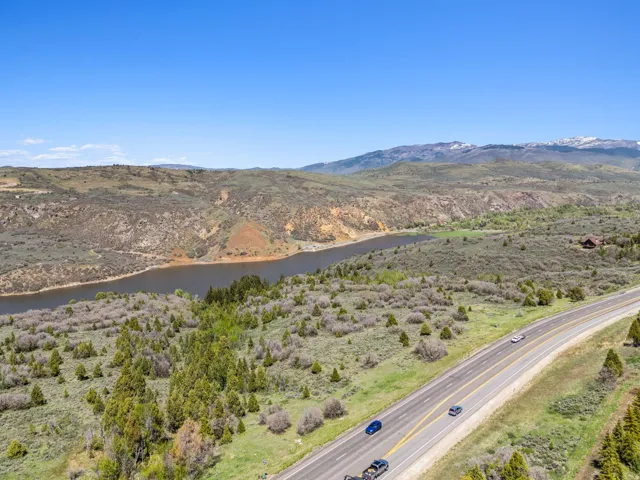 Expansive natural landscape featuring a prominent body of water, distant snow-capped mountains, and a multi-lane highway