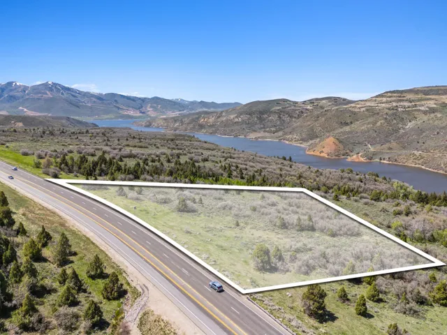 Expansive land parcel with direct road frontage, surrounded by natural vegetation, with distant mountain and water features