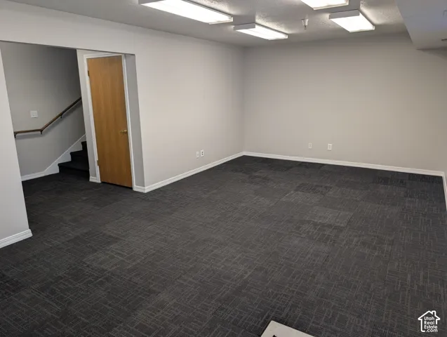 Recessed lighting fixtures, light gray wall paint, dark patterned carpet, white trim, and a wood-finish door