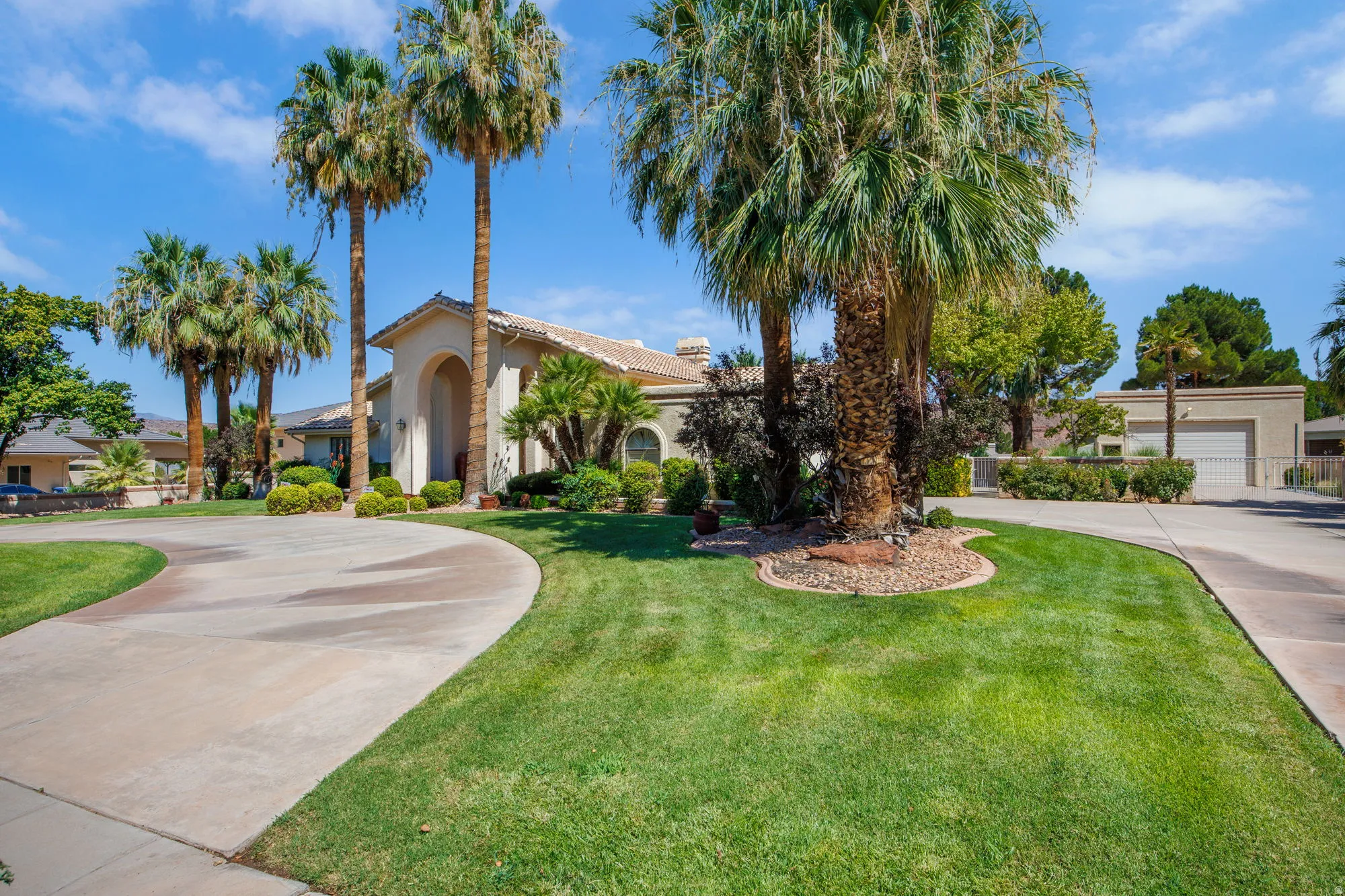 Circular driveway with a stucco exterior, mature palm trees, and a two-car garage