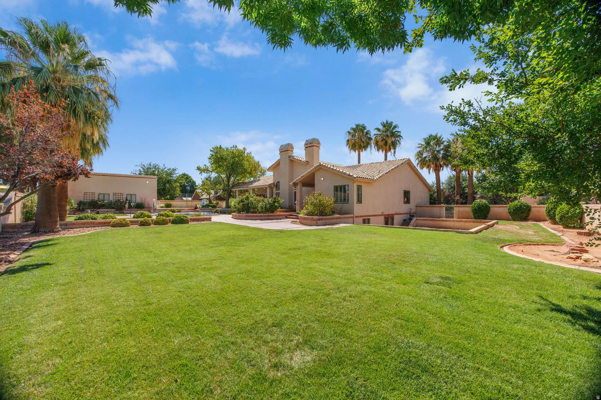 Expansive lawn with mature trees and established landscaping, surrounded by a stucco-finished residence featuring a tiled roof