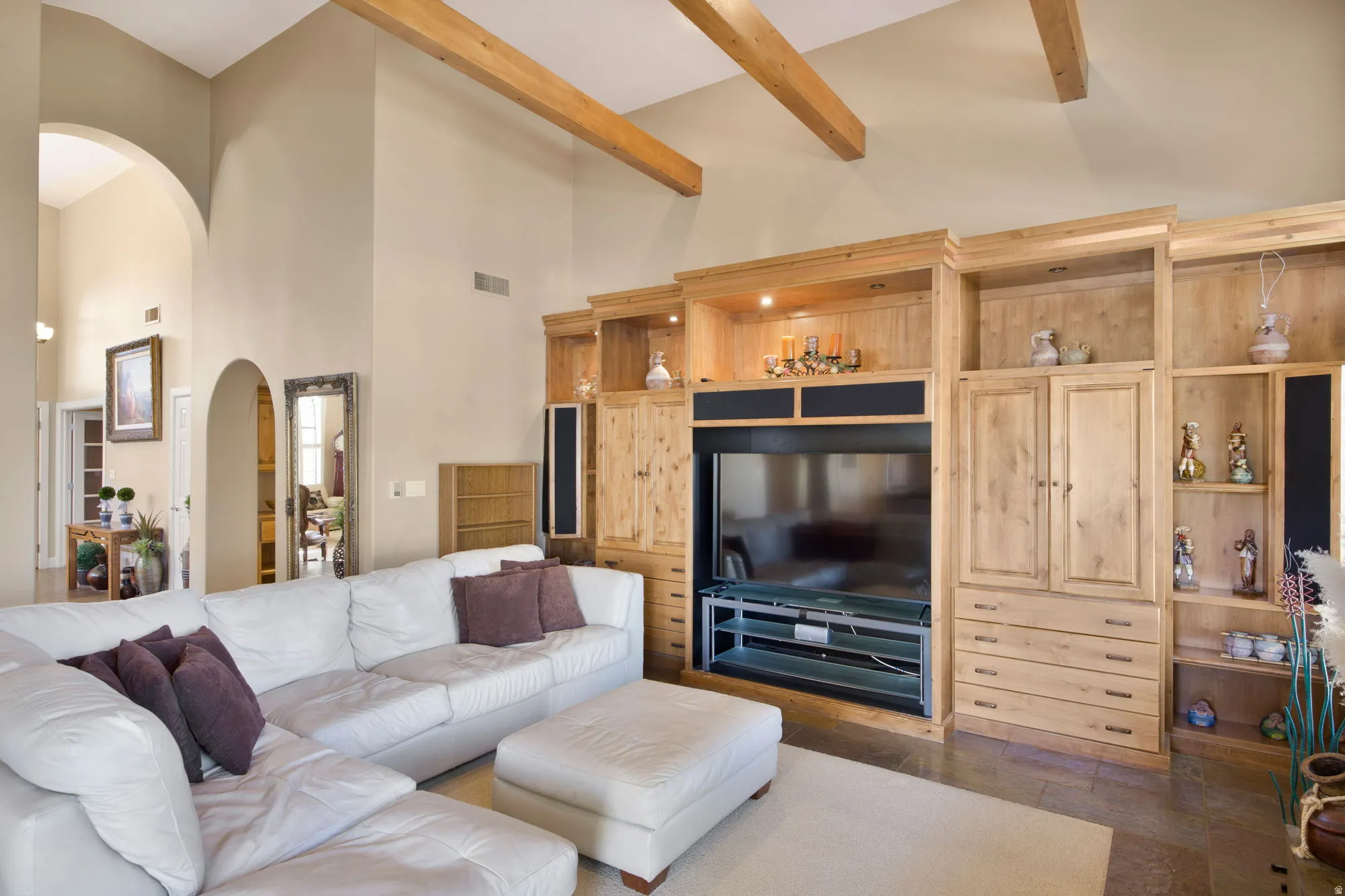 Vaulted ceilings with exposed wood beams, archway details, built-in entertainment center, custom wood cabinetry, and recessed lighting