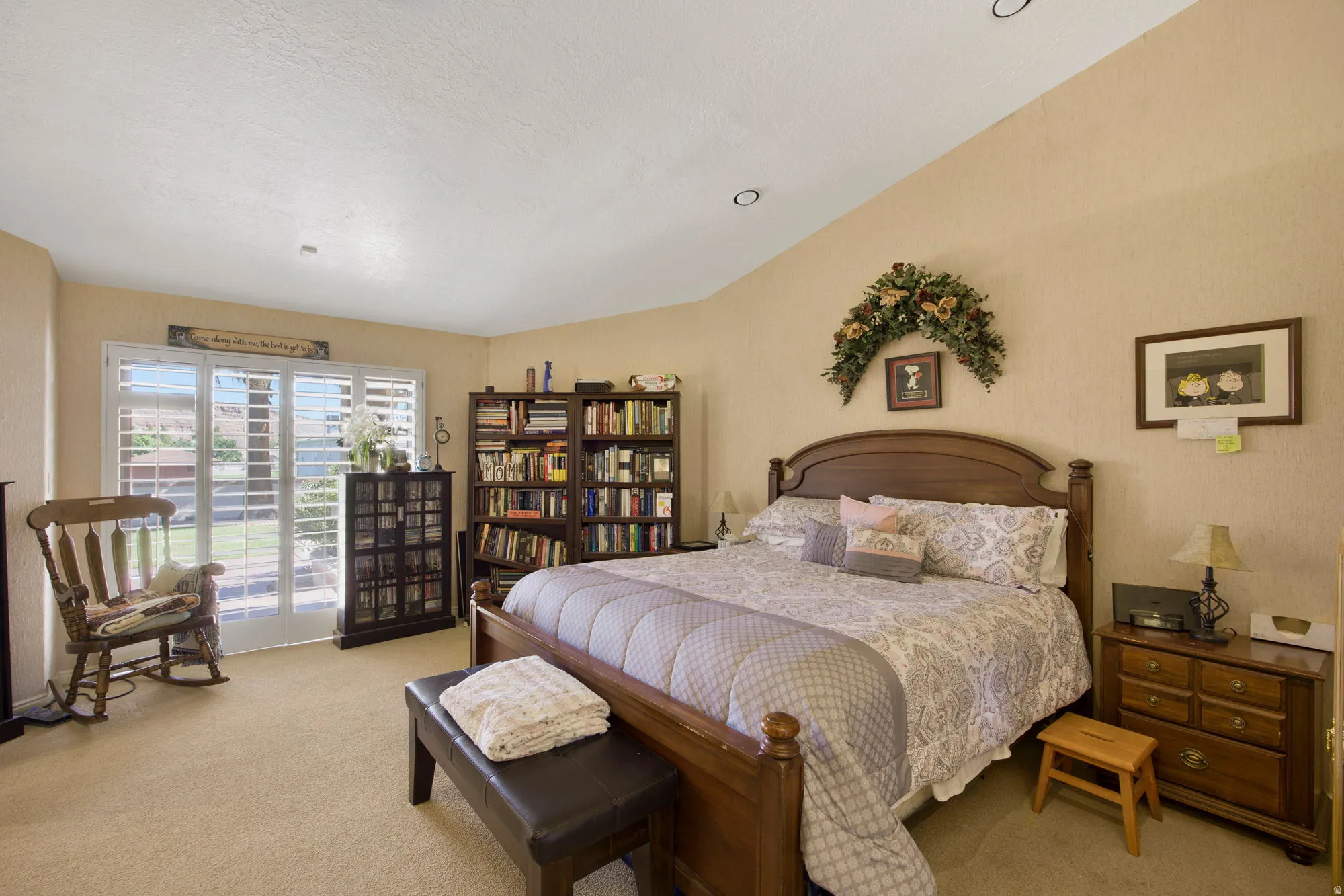 Spacious primary bedroom suite with curved ceiling detail, wood-frame bed, hardwood nightstands, built-in shelving, and glass sliding doors opening to an outdoor patio
