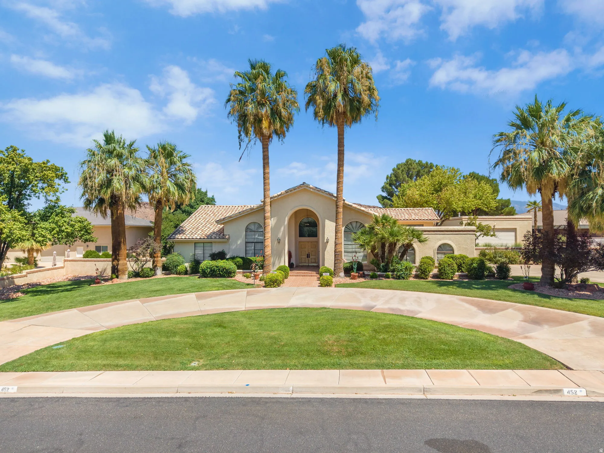 Stucco exterior with a tile roof, mature palm trees, and a circular drive