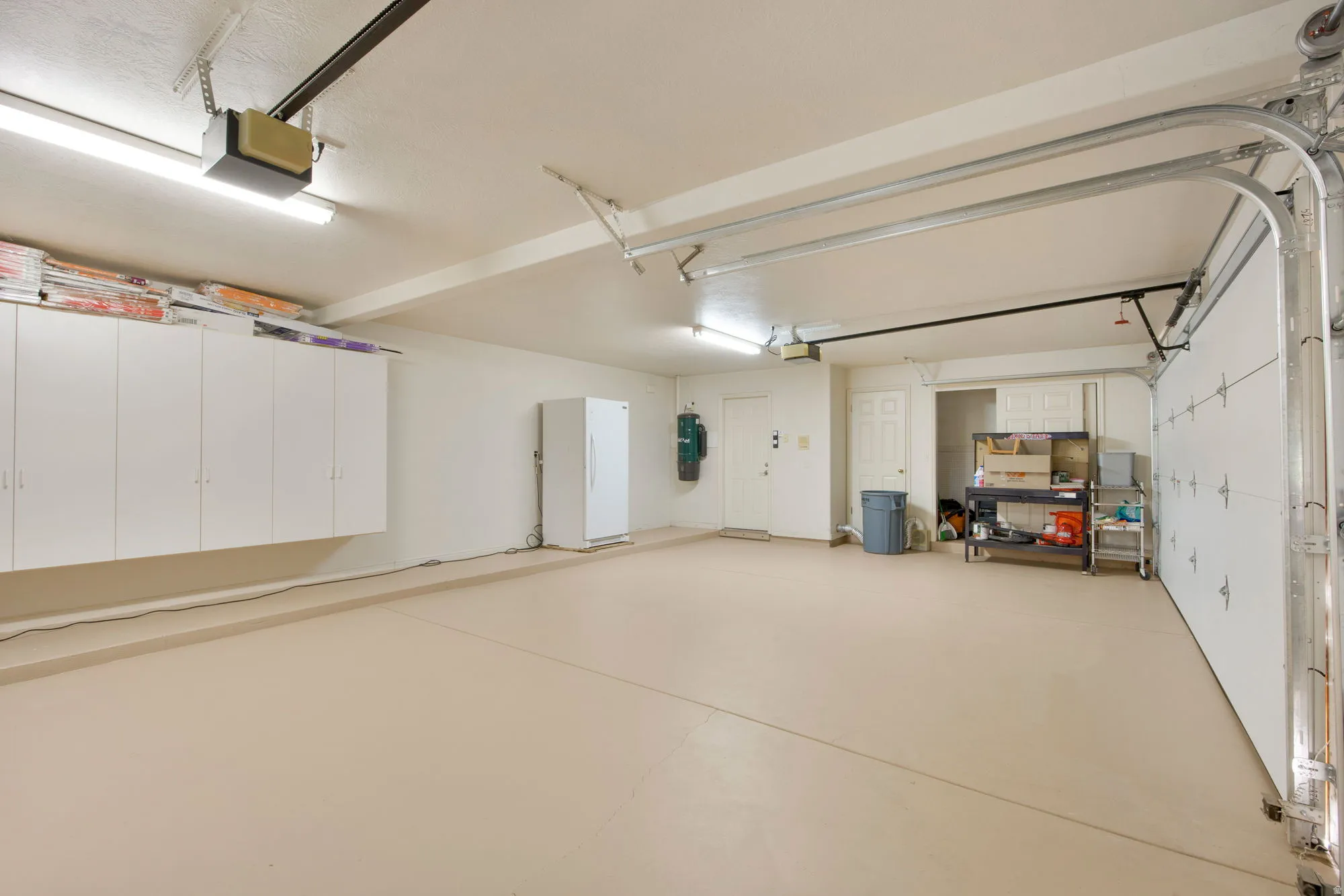 Spacious garage featuring a light-toned finished floor, extensive built-in cabinetry, dual garage door openers, and fluorescent overhead lighting