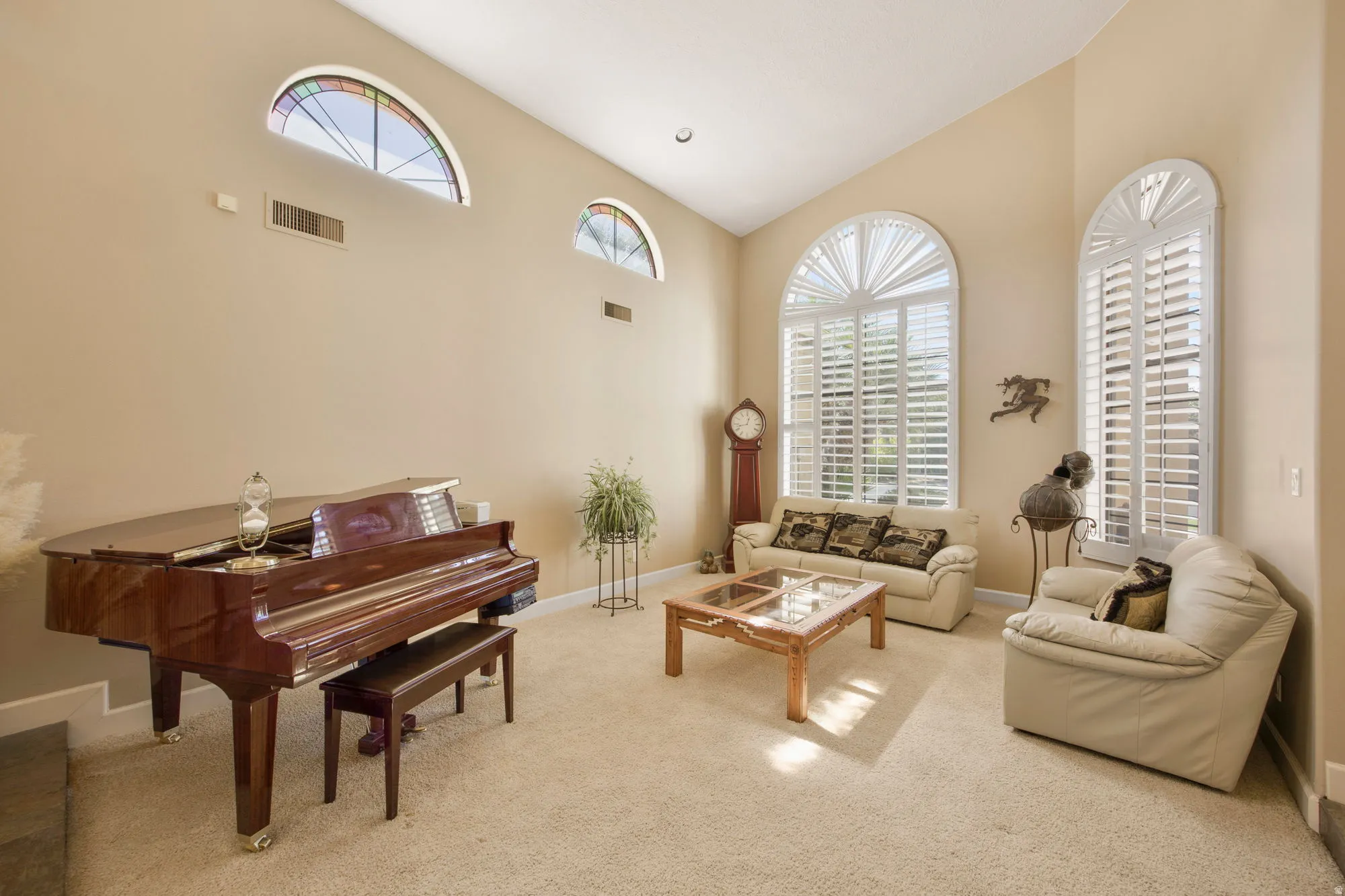 Vaulted ceiling with recessed lighting, arched windows with plantation shutters, additional arched stained-glass windows, and neutral carpeting