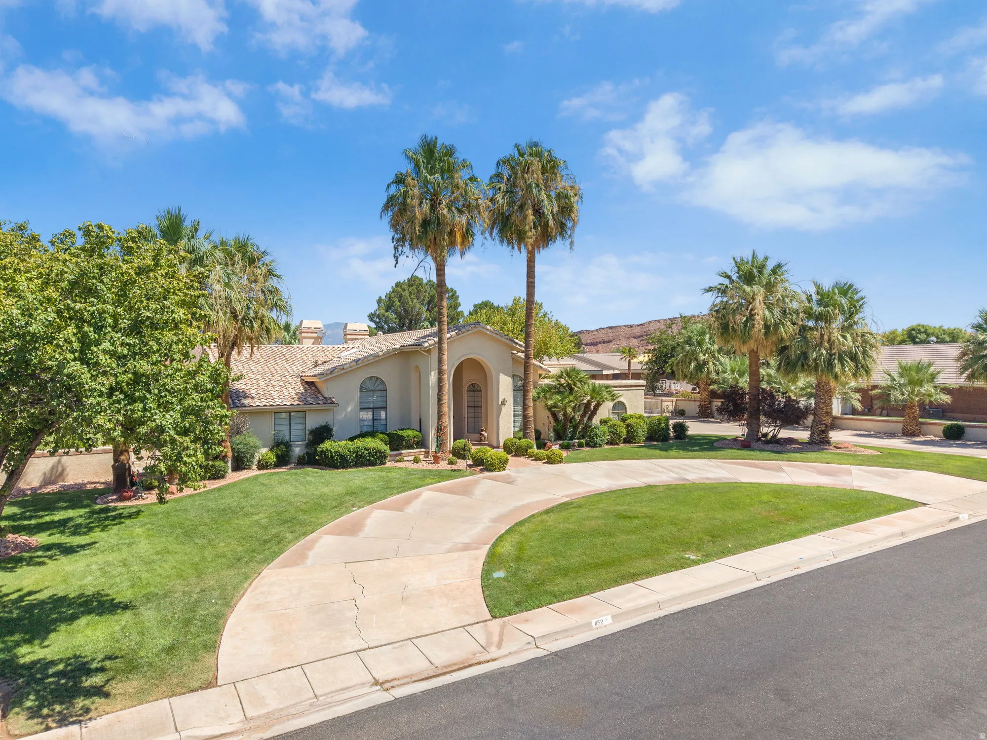 Arched entryway with a decorative door, stucco exterior, tile roof, expansive front lawn, and a circular driveway