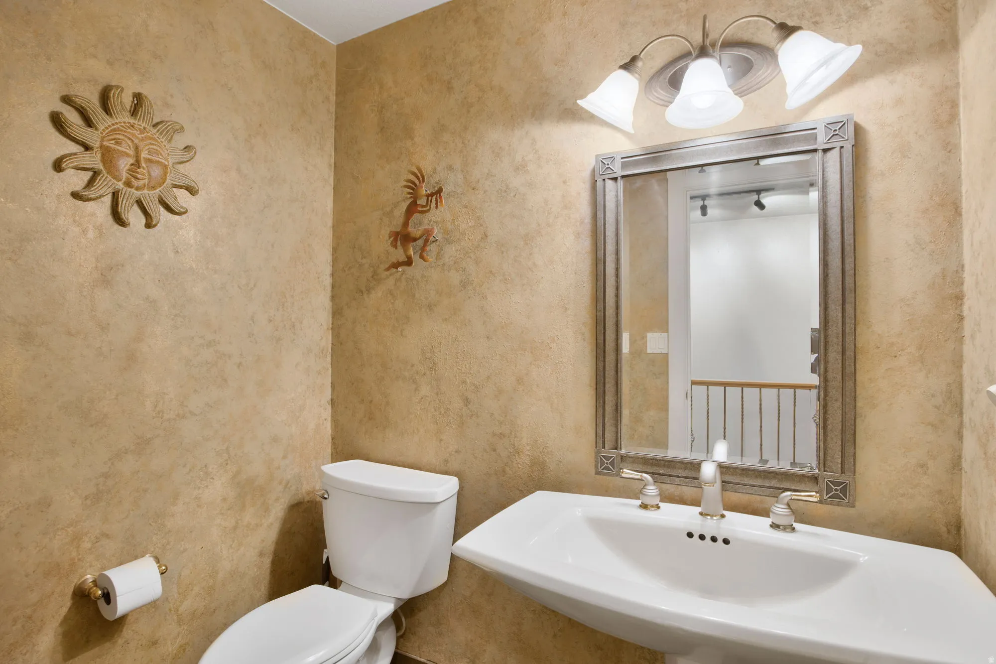 Pedestal sink with a widespread faucet, framed mirror, and a three-light vanity fixture