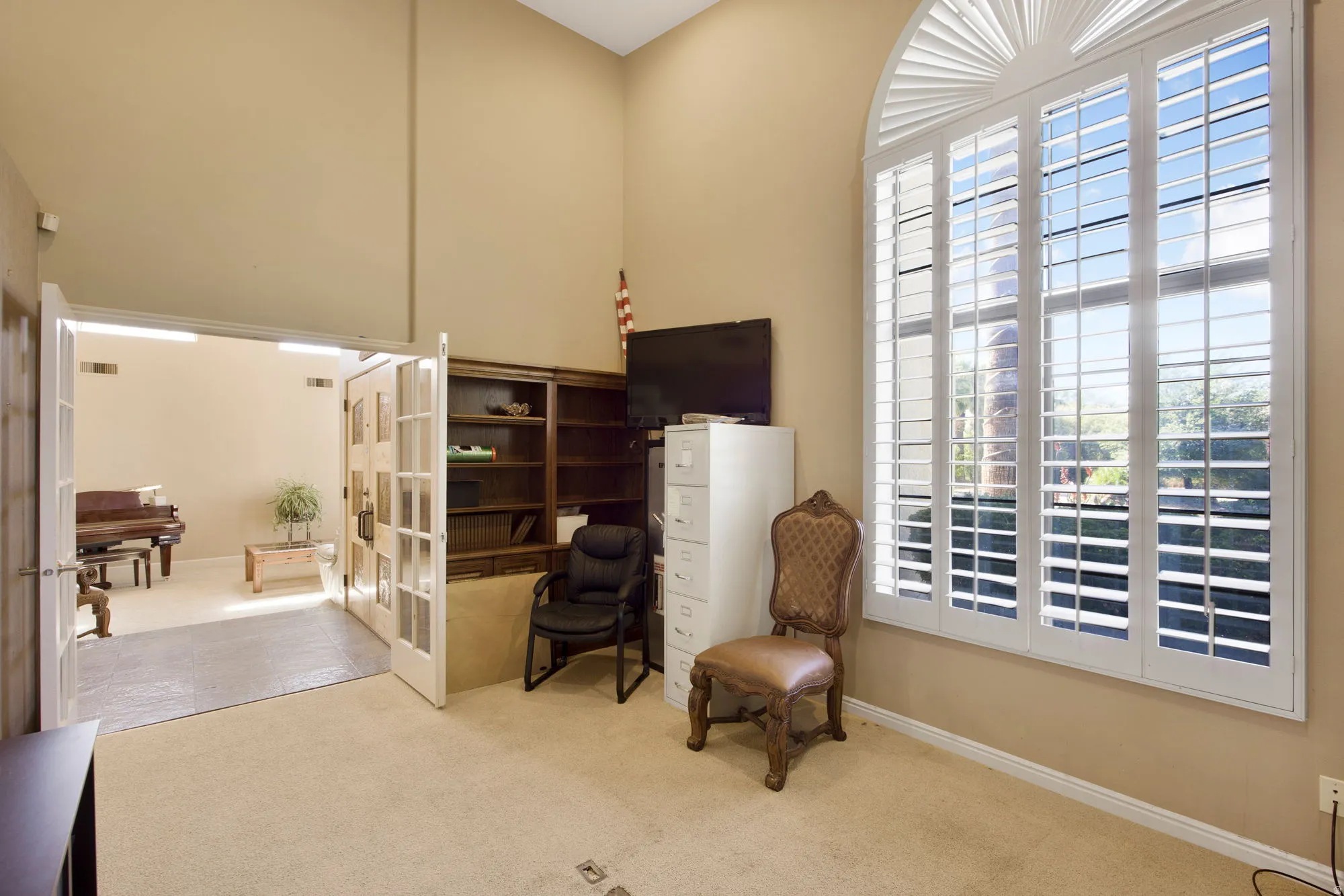 Arched window with plantation shutters, vaulted ceiling, built-in wooden shelving, and double French doors with glass panels