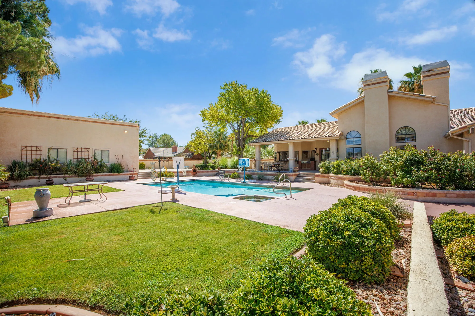 Expansive backyard oasis featuring a resort-style swimming pool with surrounding concrete decking, manicured lawn, mature landscaping including sculpted hedges and shade trees, and multiple seating areas