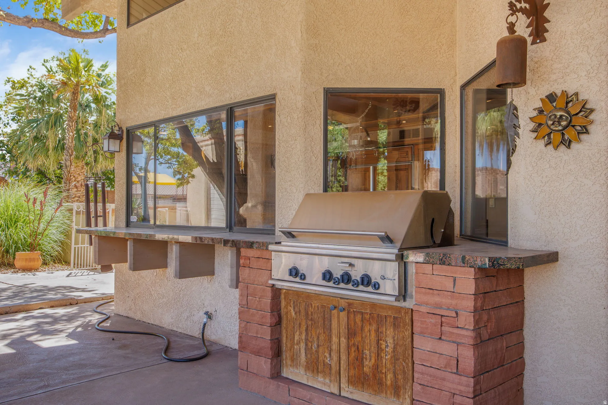 Built-in outdoor grill with stone surround, stone finish countertop, and wood-finish cabinetry