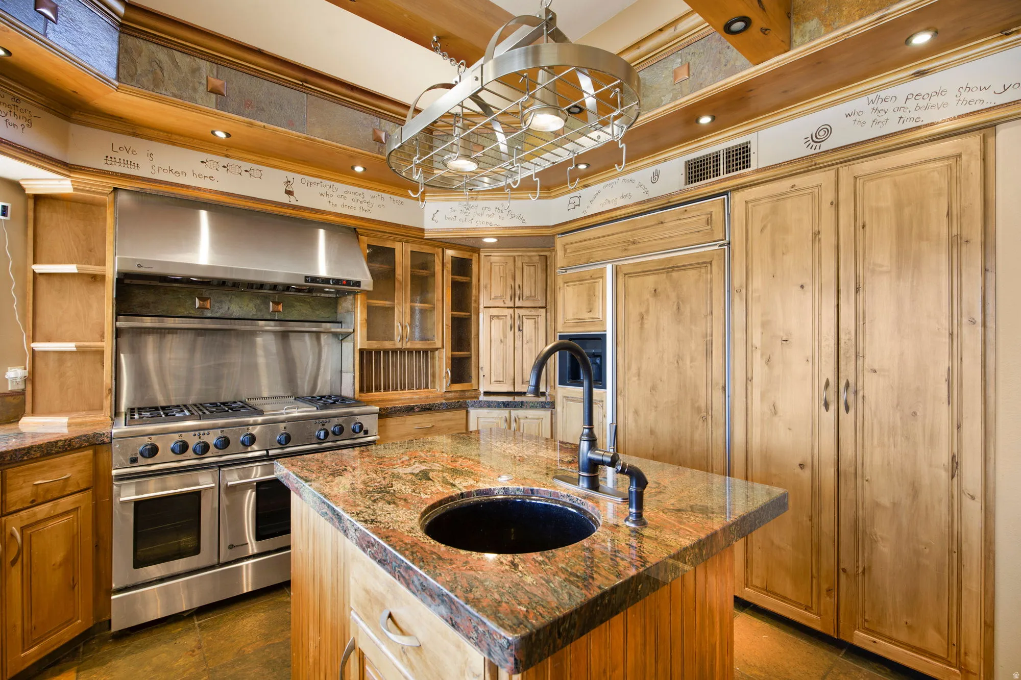 Gourmet kitchen featuring a stainless steel professional-grade range, custom wood cabinetry, a built-in pot rack, stone countertops, and a kitchen island with an integrated sink