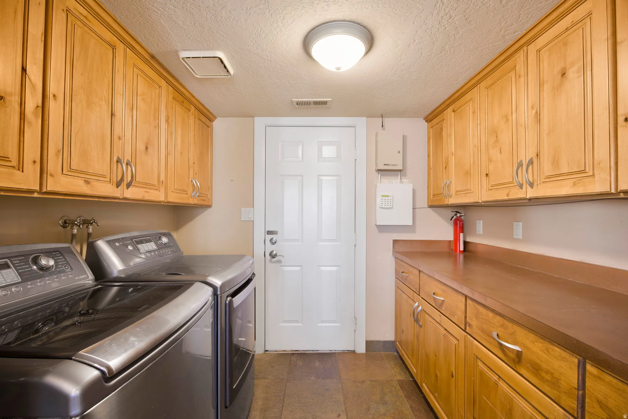 Dedicated laundry room featuring rich wood cabinetry with ample storage, stainless steel front-load washer and dryer, wood-finish countertops, and tile flooring