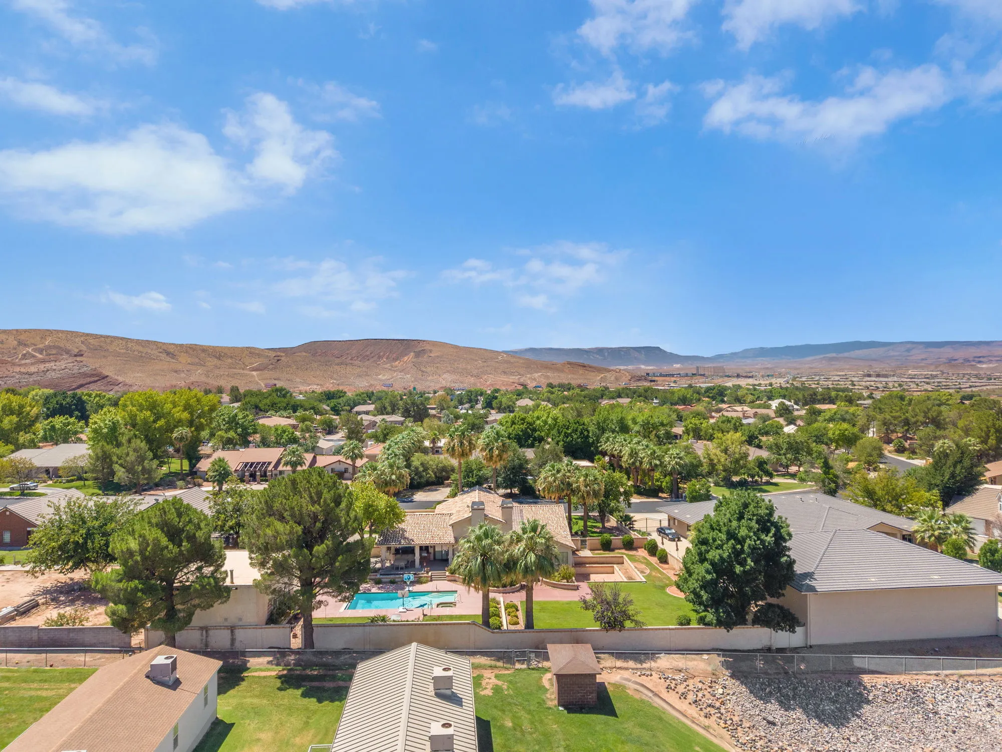 Expansive property featuring a swimming pool, mature palm trees, green landscaping, and a surrounding privacy wall