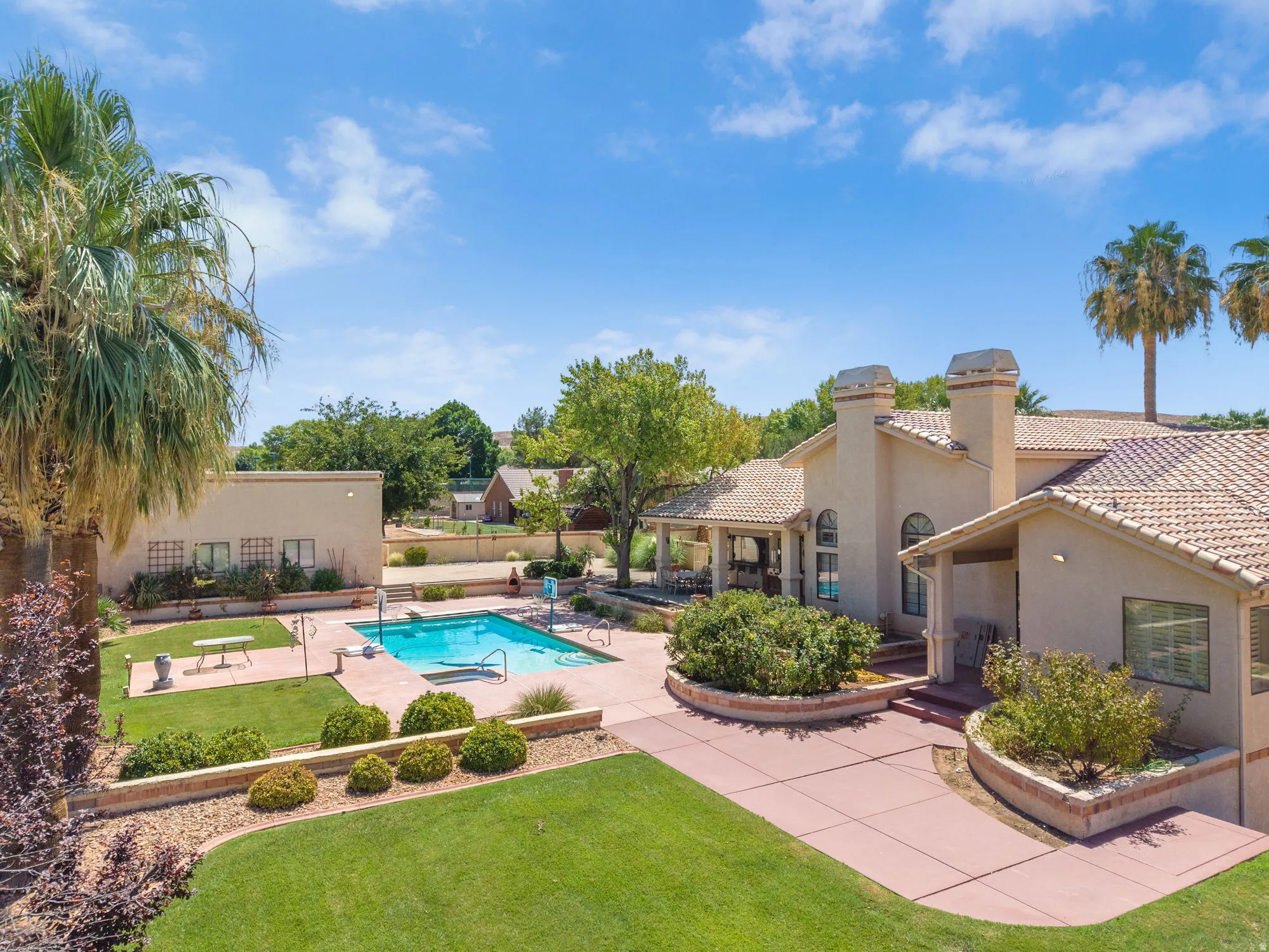 Spacious outdoor living area featuring a rectangular pool, extensive hardscaping, and manicured lawns