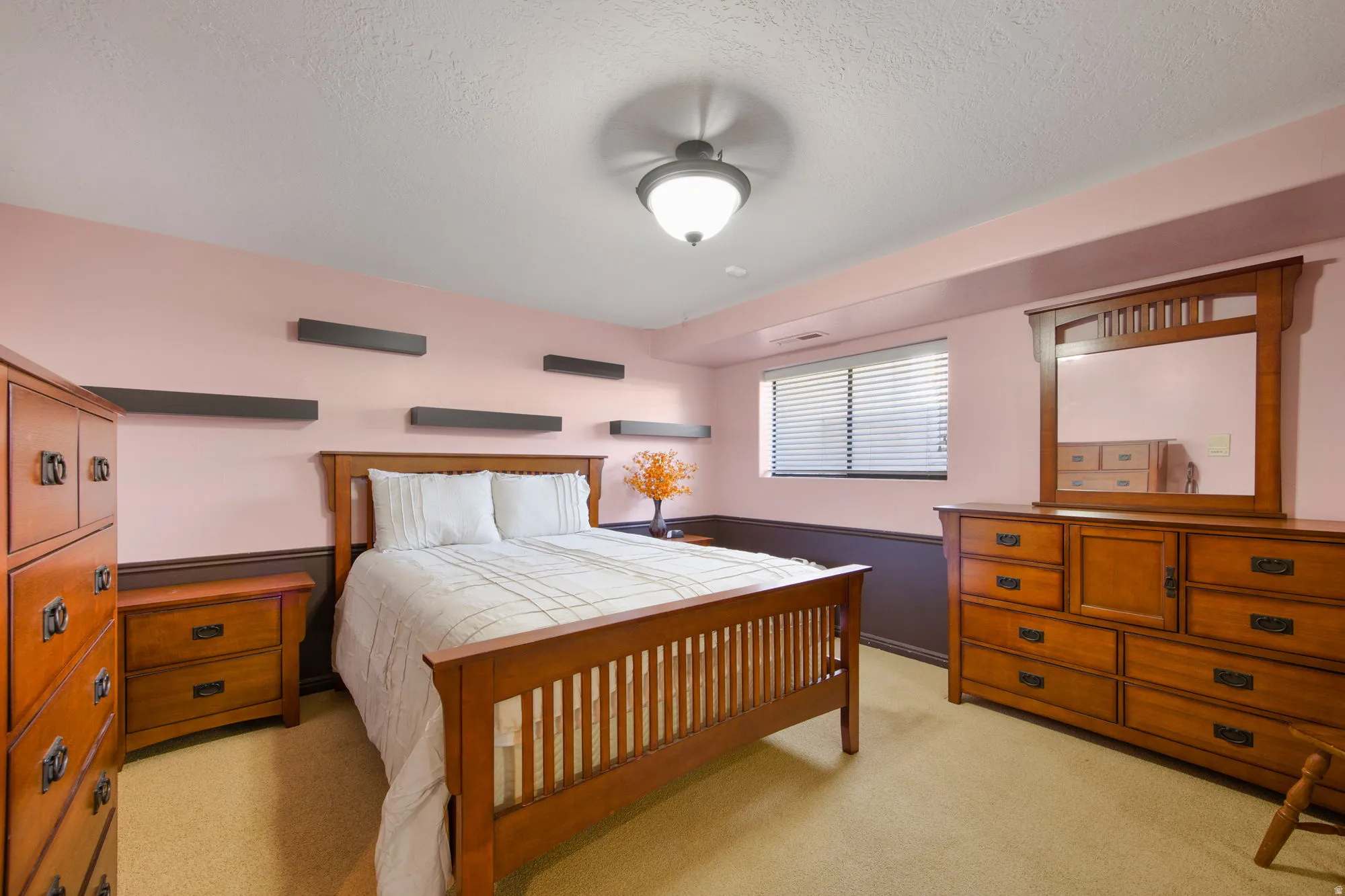 Spacious primary bedroom showcasing warm wood cabinetry, a queen-size bed frame with vertical slat detailing, soft-close drawers, and coordinating dresser with mirror