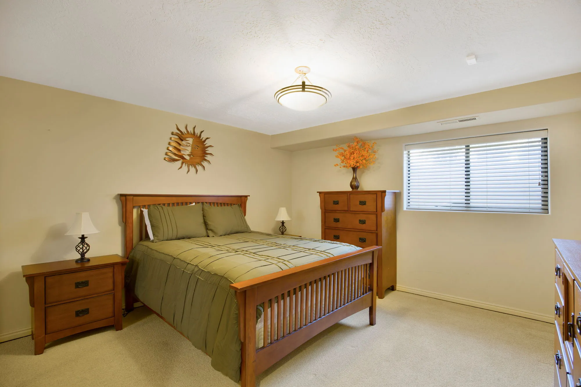 Spacious primary bedroom featuring warm wood-finish furnishings, soft neutral wall tones, and abundant natural light from dual windows with plantation shutters