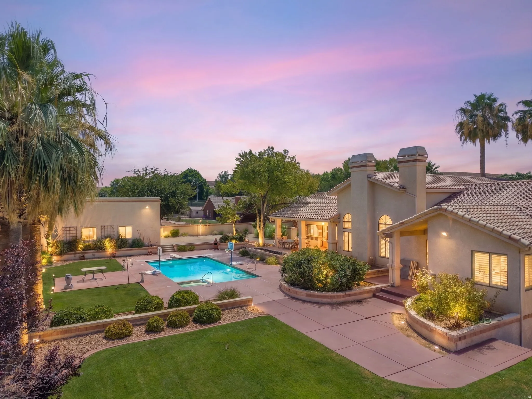Stucco exterior with tile roof, expansive patio, integrated swimming pool, mature palm trees, and manicured landscaping