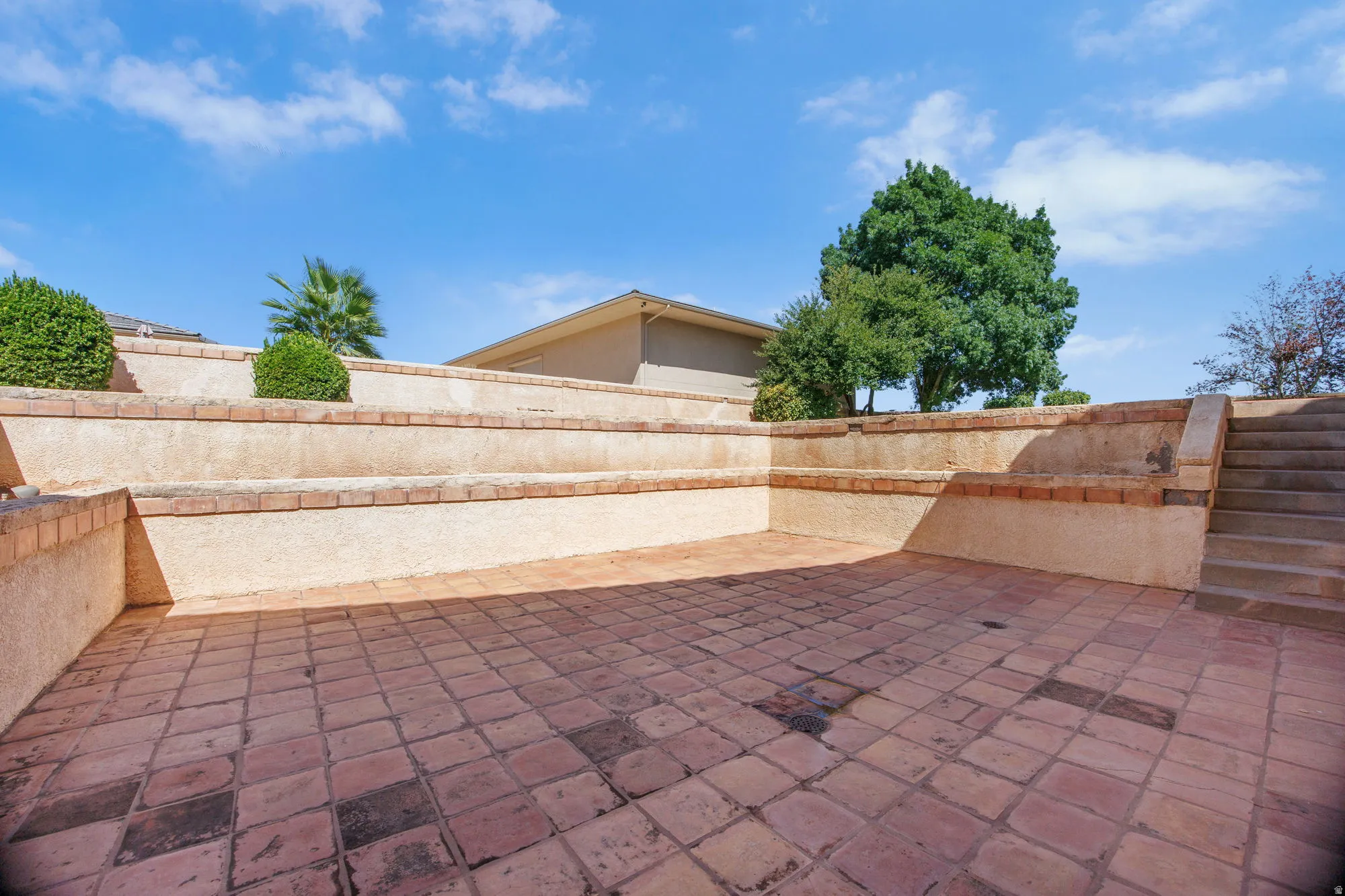 Expansive terracotta tile patio with geometric pattern detailing, enclosed by substantial stone retaining walls