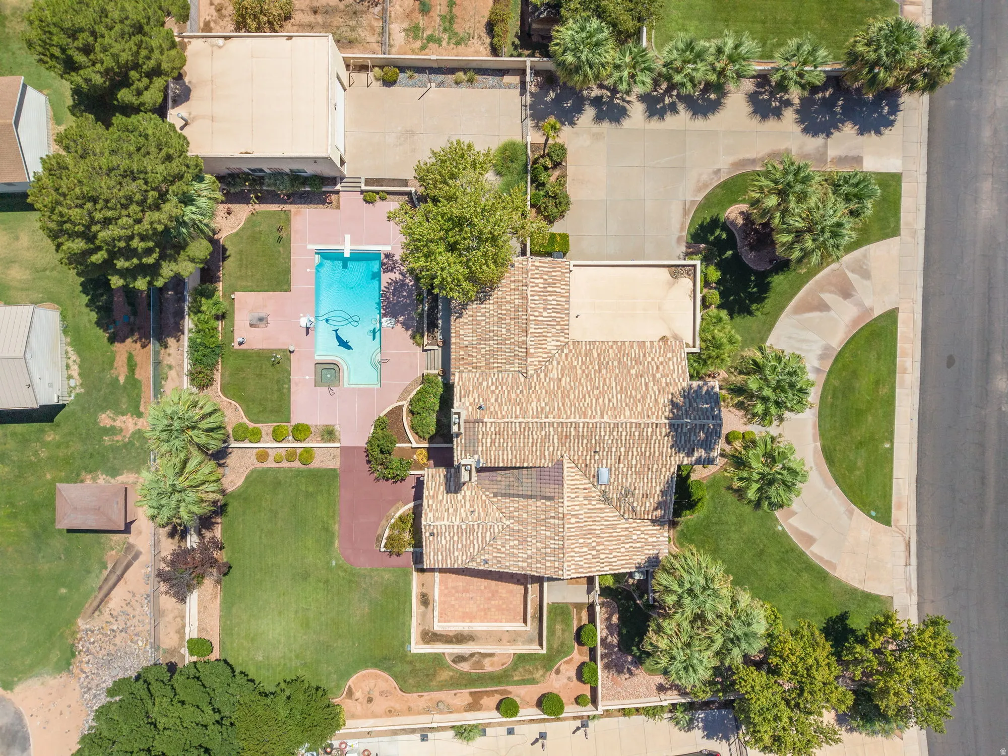 Aerial view showcasing a sprawling residential estate with mature landscaping, a resort-style swimming pool with surrounding hardscape, multiple roof lines with clay tile and composite shingle finishes, manicured lawn areas, and established trees througho