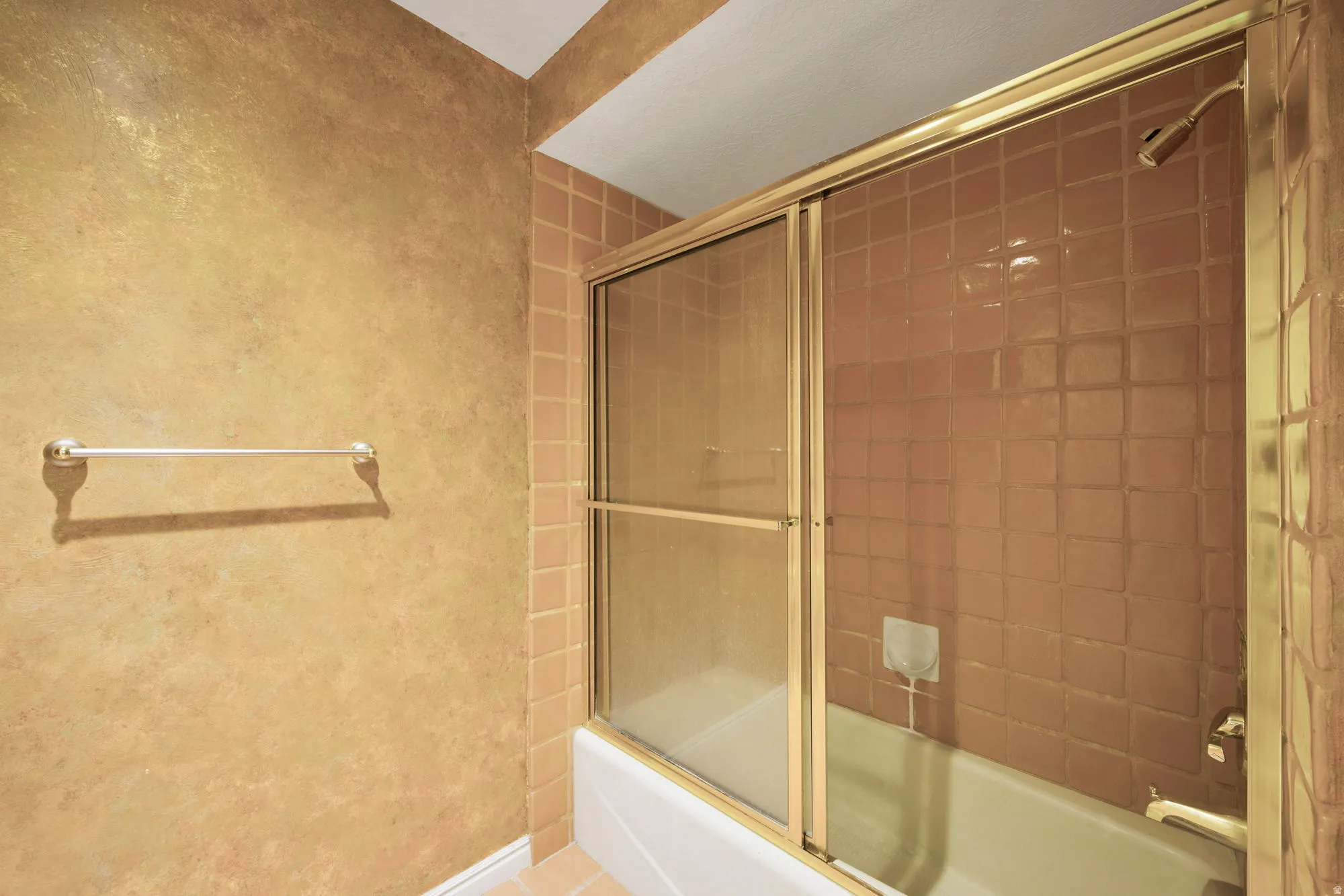 Bathtub with tile surround, sliding glass shower doors, and a gold-finish shower fixture