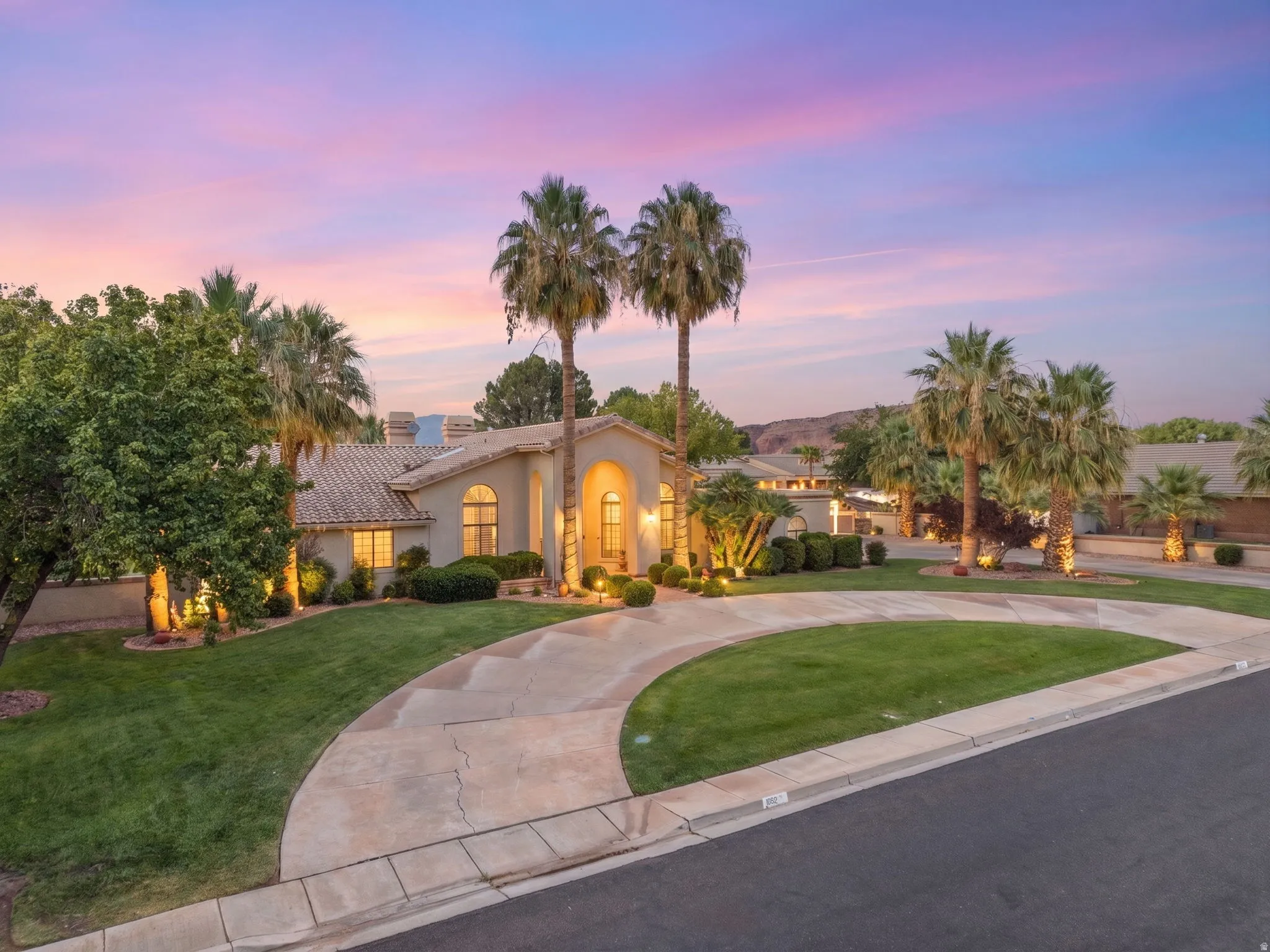 Stucco exterior with arched windows, tile roofing, and a circular concrete driveway