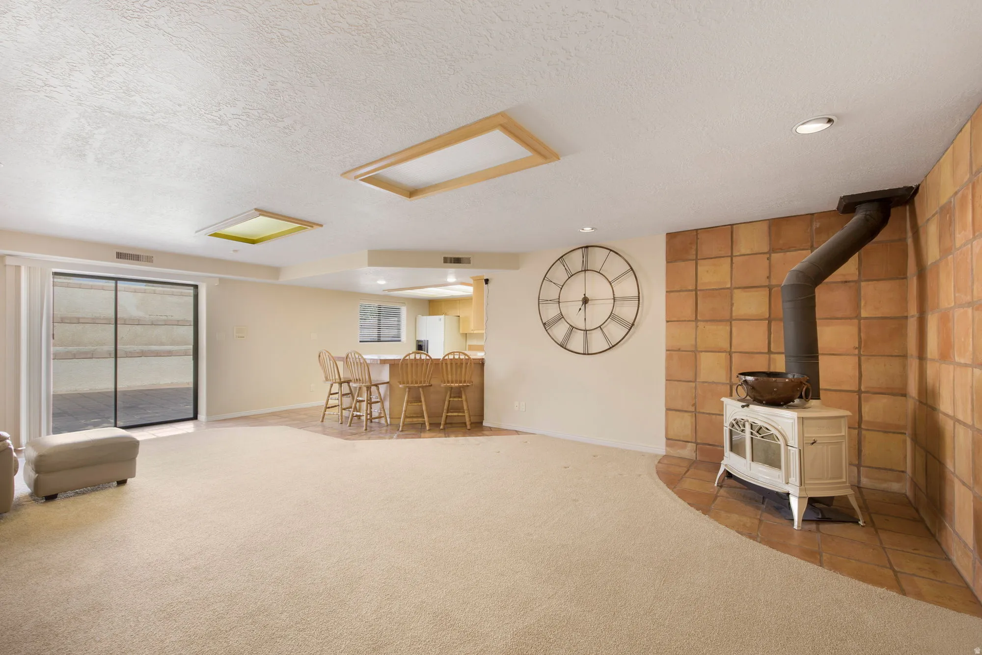 Spacious open-concept living area featuring neutral carpeting throughout, recessed ceiling lighting, and sliding glass doors with integrated blinds