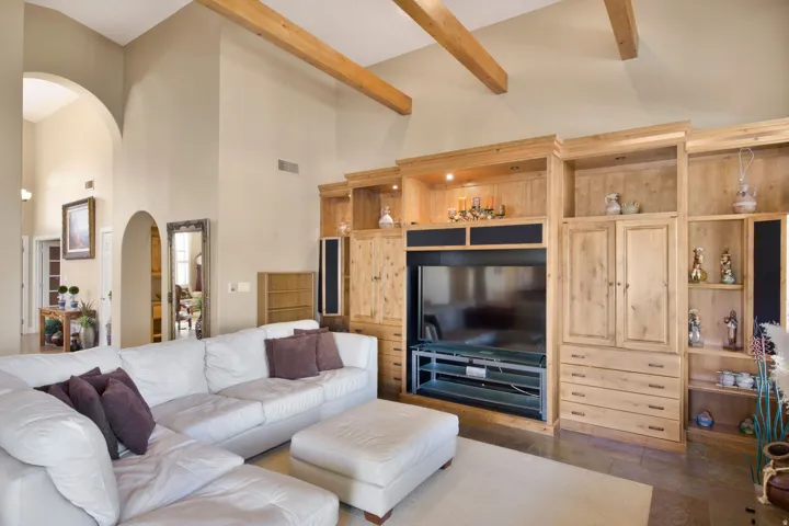 Vaulted ceilings with exposed wood beams, archway details, built-in entertainment center, custom wood cabinetry, and recessed lighting