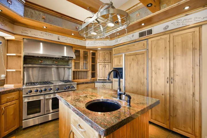 Gourmet kitchen featuring a stainless steel professional-grade range, custom wood cabinetry, a built-in pot rack, stone countertops, and a kitchen island with an integrated sink