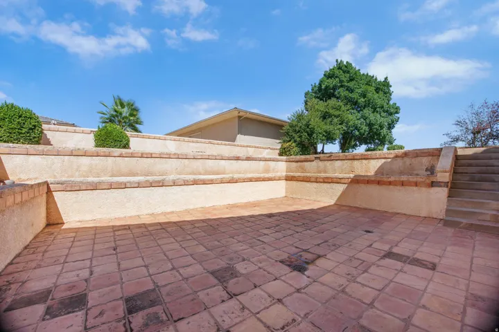 Expansive terracotta tile patio with geometric pattern detailing, enclosed by substantial stone retaining walls