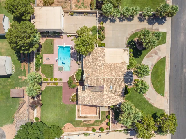 Aerial view showcasing a sprawling residential estate with mature landscaping, a resort-style swimming pool with surrounding hardscape, multiple roof lines with clay tile and composite shingle finishes, manicured lawn areas, and established trees througho