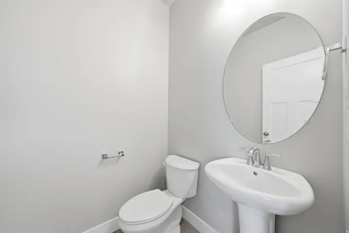 Pedestal sink with chrome fixtures, oval wall mirror, and a white toilet