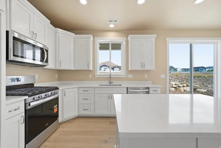 Kitchen featuring white cabinetry, stainless steel appliances, light-toned countertops, wood-finish flooring, and recessed lighting