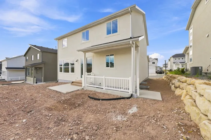 Rear exterior featuring a covered porch with white railings, concrete patio, and a stone retaining wall