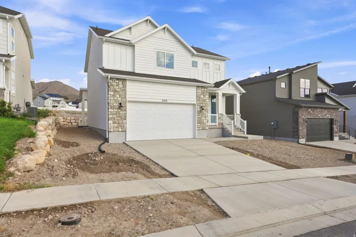 Two-story residence featuring a stone and siding exterior, an attached two-car garage, and a covered front porch