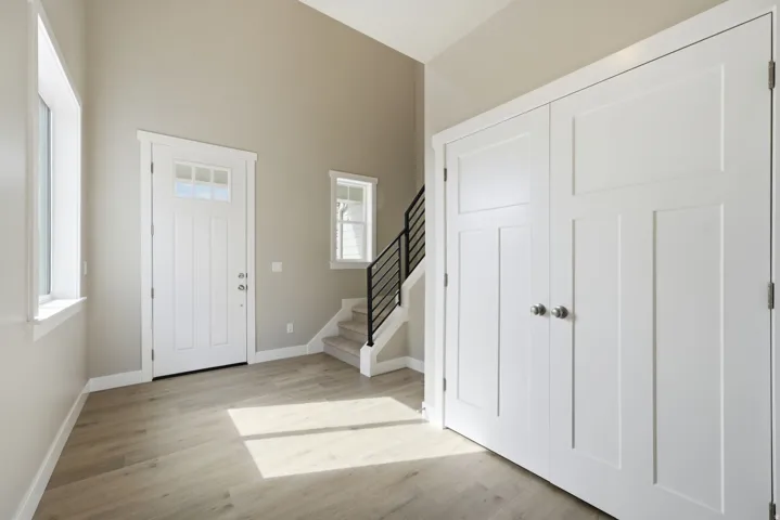 Entryway featuring a vaulted ceiling, wood-finish flooring, white panel doors, and a staircase with a black metal railing